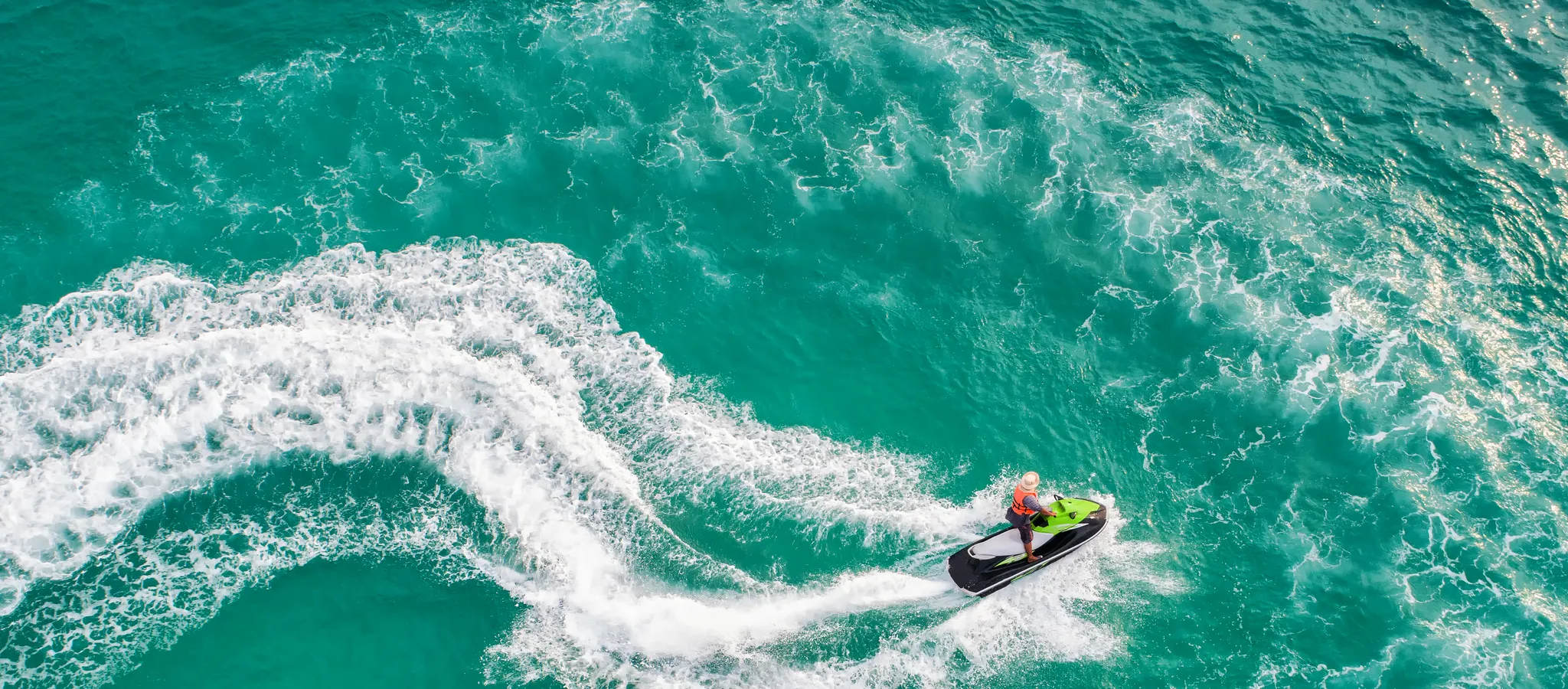 A person ejoying fun times on a jet ski in the sea. Aerial view. The color of the water... clear turquoise at tropical beach. An estate and wealth themed stock photo.