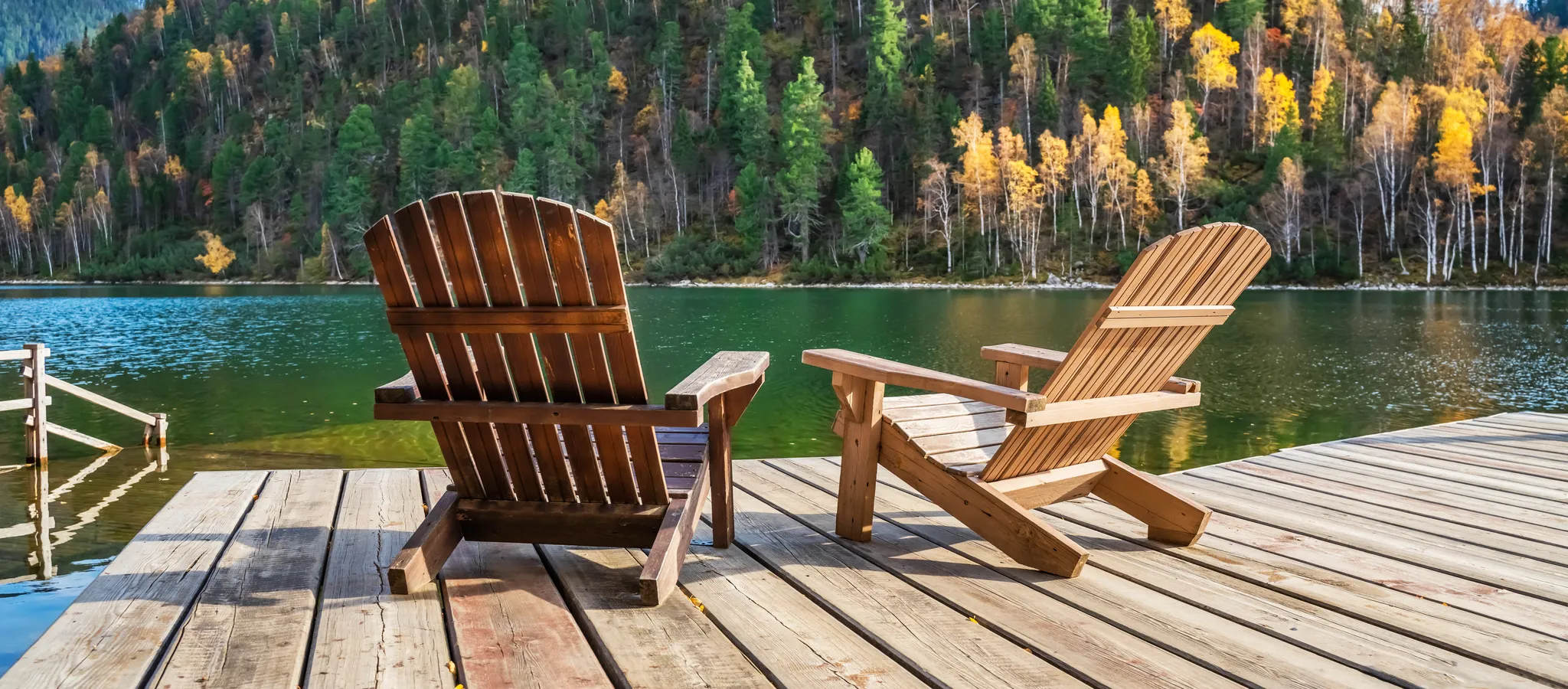 Two Adirondack chairs on a wooden dock overlooking a calm lake, beautiful landscape of mountain lake, vacation in the mountains, luxury autumn vacation concept. Perhaps an estate and wealth themed stock photo.