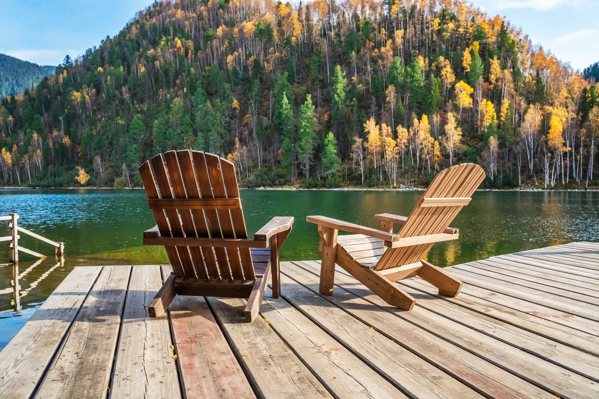 Two Adirondack chairs on a wooden dock overlooking a calm lake, beautiful landscape of mountain lake, vacation in the mountains, luxury autumn vacation concept. Perhaps an estate and wealth planning themed stock photo.